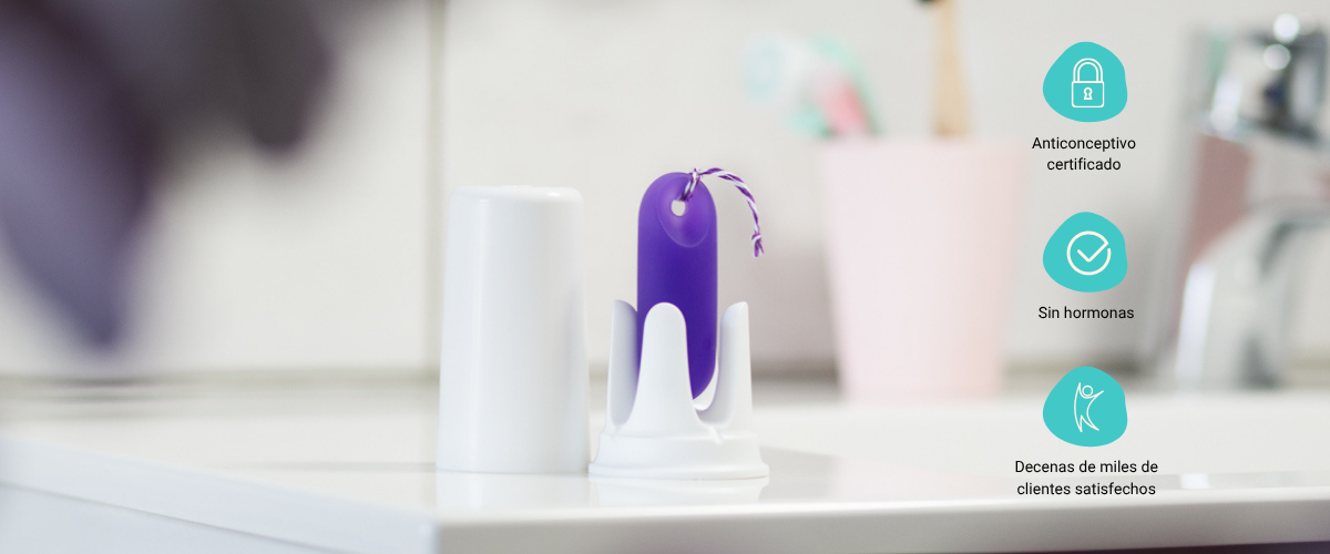 Sensor menstrual trackle morado con su base y tapa blanca en el baño, con iconos informativos que destacan sus ventajas: anticonceptivo certificado, sin hormonas y decenas de miles de clientes satisfechos.