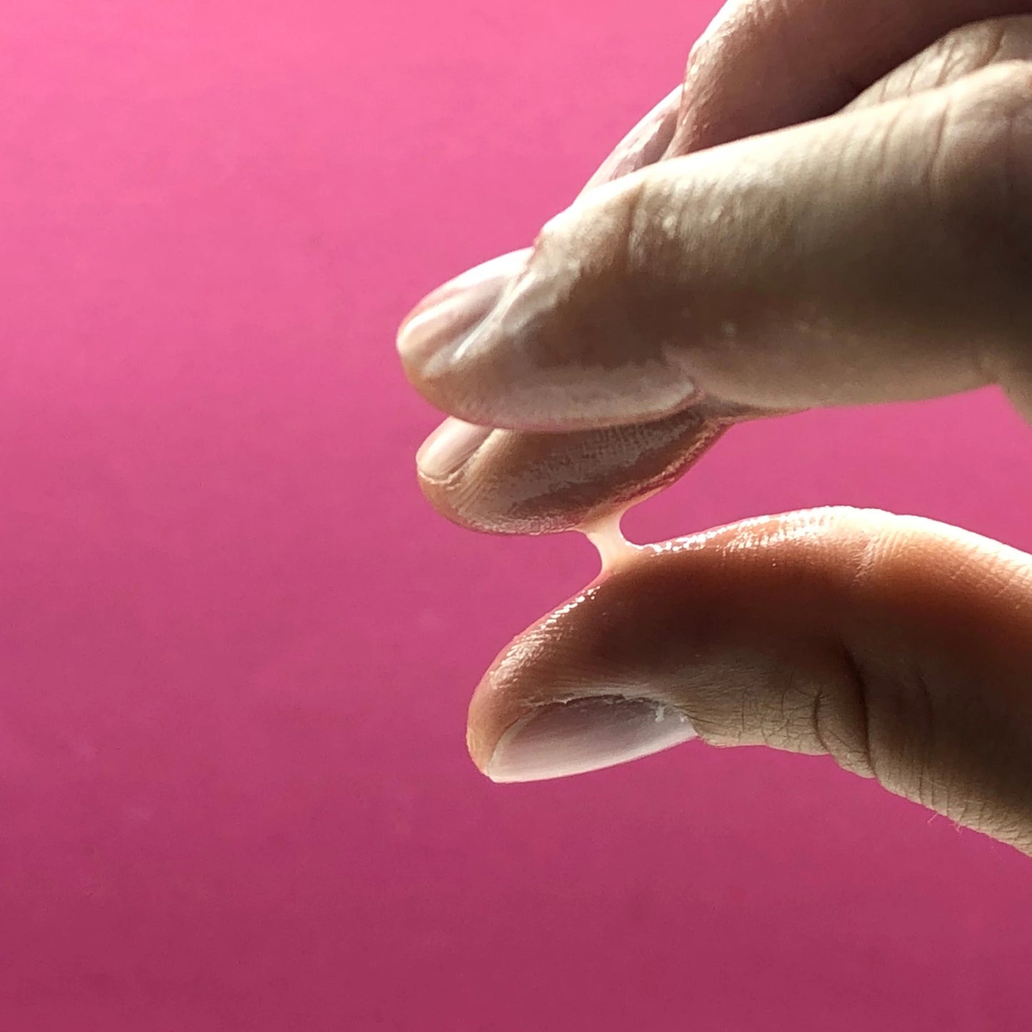 Imagen para determinar la fertilidad: se comprueba la capacidad de formar hilos del moco cervical entre el pulgar y el índice. El moco forma un hilo bien definido, lo que indica la fase de mayor fertilidad del ciclo menstrual. Fondo de color rosa.