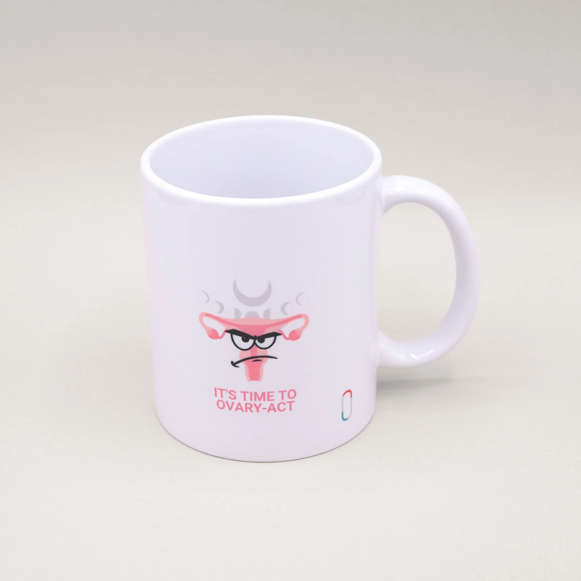 Weiße trackle Tasse mit einem humorvollen Design: Ein illustrierter Uterus mit Angry-Face-Gesichtsausdruck, verziert mit rosa Blüten und angedeuteten Mondphasen. Darunter steht der pinke Schriftzug 'IT'S TIME TO OVARY-ACT'. Das trackle-Logo ist unten rechts sichtbar.