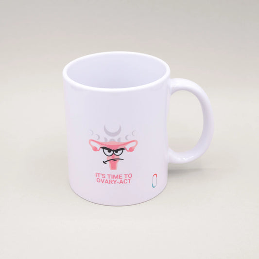 Weiße trackle Tasse mit einem humorvollen Design: Ein illustrierter Uterus mit Angry-Face-Gesichtsausdruck, verziert mit rosa Blüten und angedeuteten Mondphasen. Darunter steht der pinke Schriftzug 'IT'S TIME TO OVARY-ACT'. Das trackle-Logo ist unten rechts sichtbar.