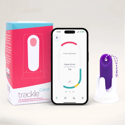 trackleCatch: Die rosa-weiße Verpackung des Sensorsystems steht neben einem Smartphone, das die trackle App mit der Statusmeldung 'Heute ist ein unfruchtbarer Tag' zeigt. Rechts daneben ist der lila trackleCatch mit lila-weißer Rückholkordel in seiner Halterung abgebildet.