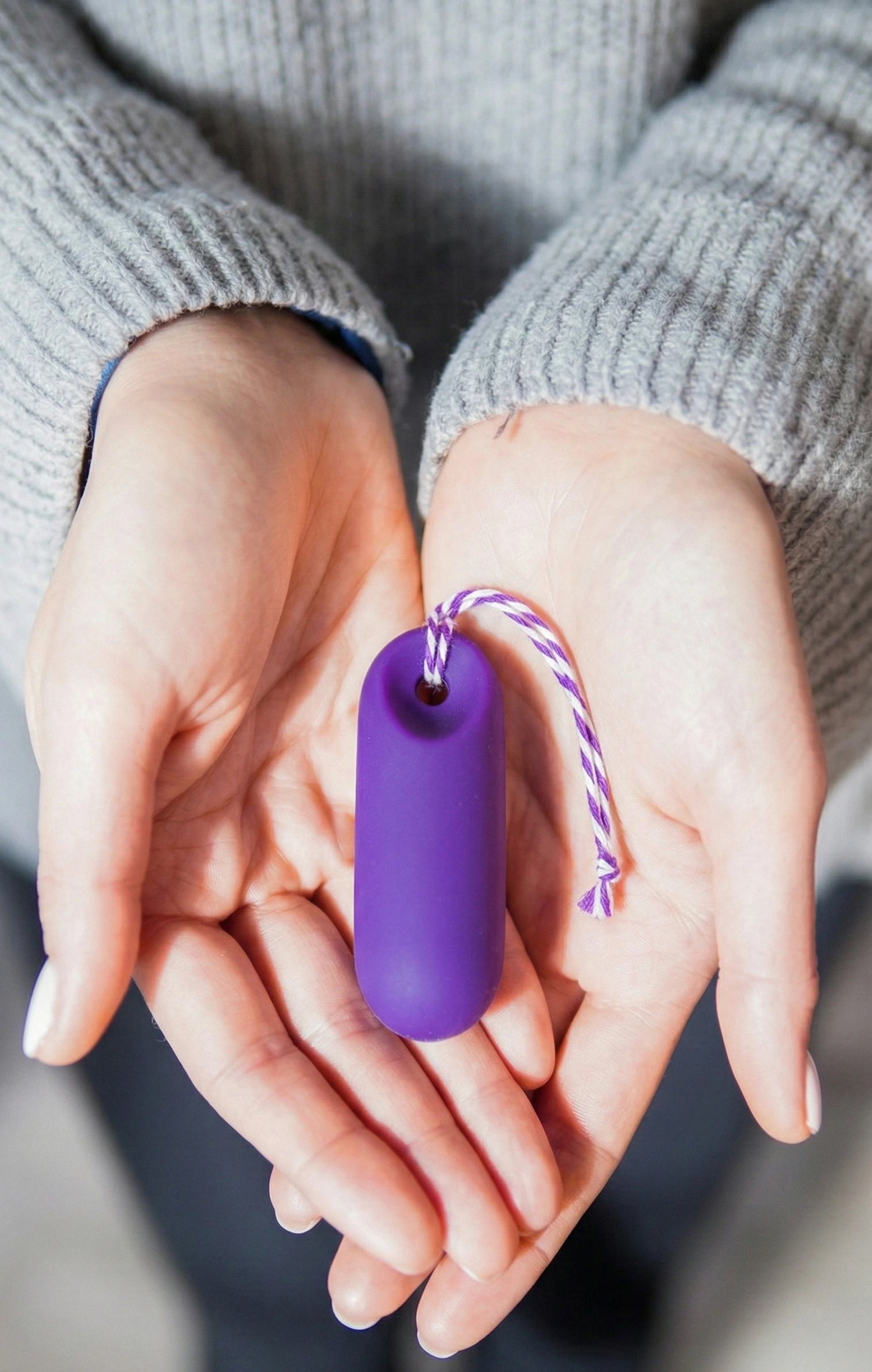 Nahaufnahme: Der lila trackleCatch liegt in zwei geöffneten Handflächen. Die Aufnahme zeigt die kompakte Größe und die glatte Oberfläche des Sensors sowie die lila-weiß gestreifte Rückholkordel. Eine persönliche und greifbare Darstellung des Geräts.