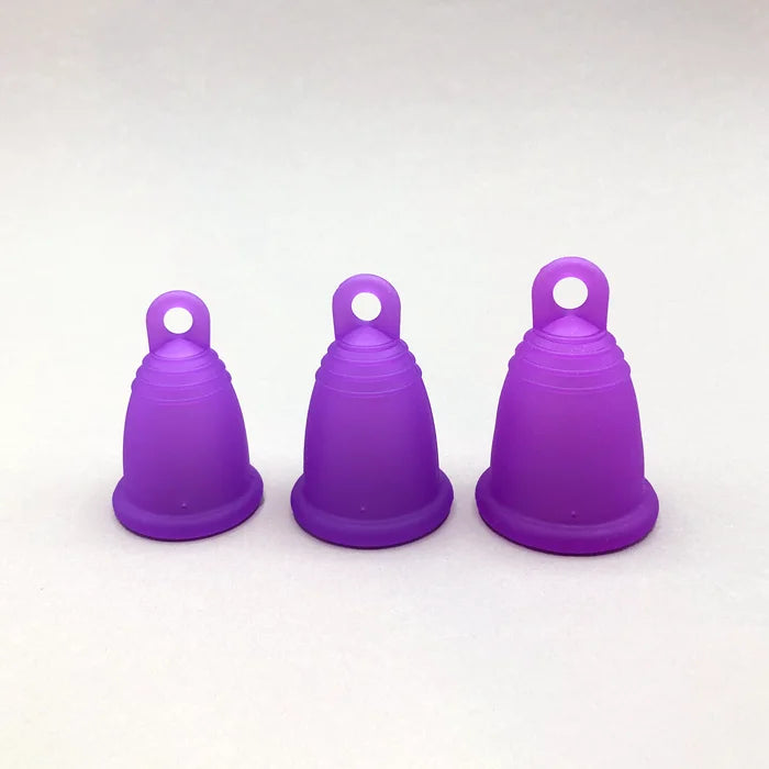 Drei lila trackleCup Menstruationstassen in den Größen S, M und L stehen zum Vergleich nebeneinander. Die Cups haben eine ergonomische Form mit einer praktischen Ring-Griffhilfe am Boden für einfaches Entfernen.