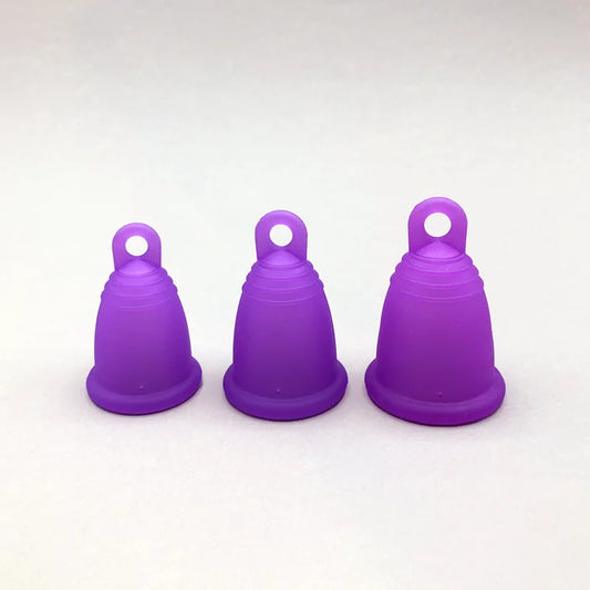 Drei lila trackleCup Menstruationstassen in den Größen S, M und L stehen zum Vergleich nebeneinander. Die Cups haben eine ergonomische Form mit einer praktischen Ring-Griffhilfe am Boden für einfaches Entfernen.